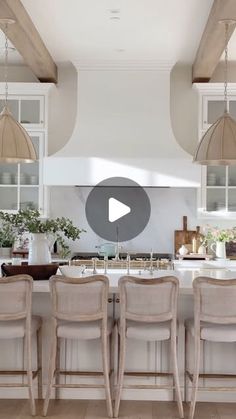 a large kitchen with white cabinets and counter tops, along with four beige bar stools