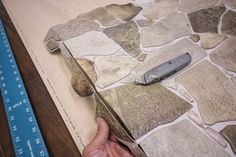 a person is using a knife to cut out stone tiles on a table with a ruler