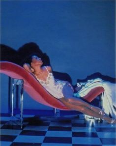 a woman laying on top of a red chair next to a black and white checkered floor