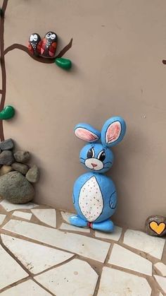 a blue bunny sitting on top of a tiled floor next to rocks and a tree