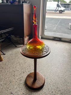 a colorful glass vase sitting on top of a wooden stand in front of a window