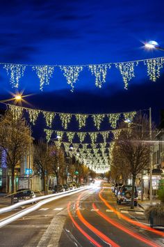 a city street at night with christmas lights strung over the road and cars passing by