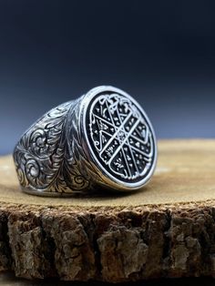 a silver ring sitting on top of a piece of wood with an intricate design in the middle