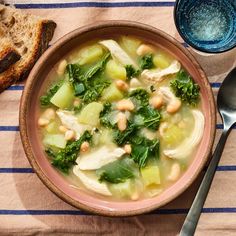 a bowl of chicken and vegetable soup next to some bread on a blue and white table cloth