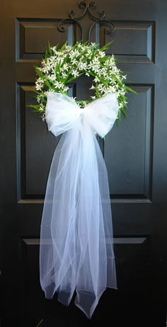 a wreath with white flowers hanging on the front door to decorate it for someone's special occasion