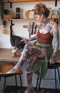 a woman with tattoos sitting on a stool next to a cat