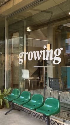 three green chairs sitting in front of a glass window with the word growing written on it