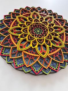 an intricately designed paper plate on a white surface with colored lines in the shape of a flower