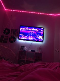 a television that is on in the corner of a room with pink lights around it