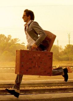 a man running down the street with a suitcase in his hand and an elephant behind him