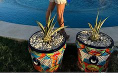 a woman standing next to two large potted plants in front of a swimming pool