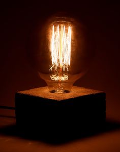 a glowing light bulb sitting on top of a block of wood in the dark room