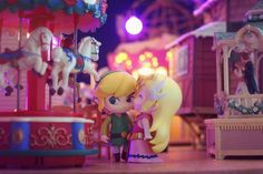 two toy figurines standing next to each other in front of a carousel