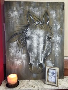 a painting of a horse on a wooden board next to a lit candle with a picture frame