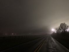 a foggy road at night with trees on both sides and lights in the distance