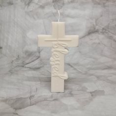 a white cross shaped candle with the word jesus written in cursive writing on it