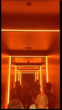 a group of people walking down a hallway with orange lights on the ceiling and walls