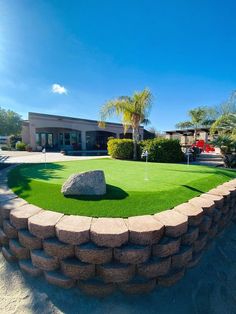 an artificial lawn in front of a building with a rock on the grass and palm trees