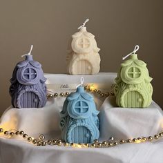 three small ceramic houses are on a white tablecloth with beads and lights around them