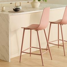 two pink barstools sitting on top of a wooden floor next to a counter