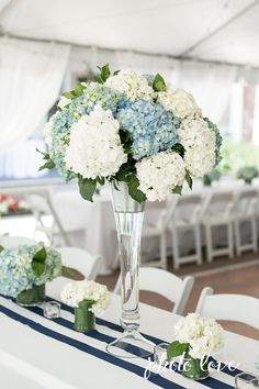 a vase filled with white and blue flowers on top of a table covered in chairs