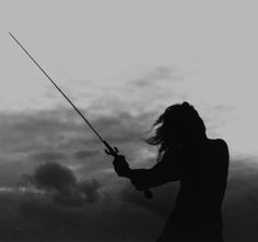 a woman holding a fishing pole while standing on top of a beach next to the ocean