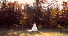 a woman in a white dress is walking through the grass with trees behind her and an orange sky