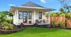 a small white house sitting in the middle of a lush green yard next to a wooden fence