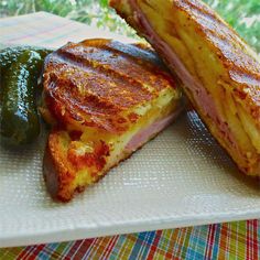 two pieces of ham and cheese sandwich on a plate with pickles next to it