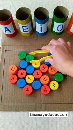 a person cutting out letters with scissors on top of a cardboard box filled with markers