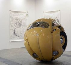 a large yellow car sitting on top of a floor next to a white wall with drawings behind it