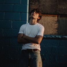 a man standing in front of a blue brick wall with his arms crossed and eyes closed