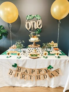 a table topped with balloons and cake next to a sign that says one happy birthday