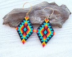 a pair of colorful beaded earrings sitting on top of a piece of driftwood