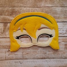 a yellow and white mask with black eyes on a wooden surface next to a piece of wood