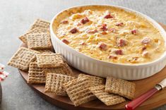 a bowl of dip surrounded by crackers on a cutting board