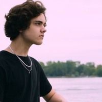 a young man standing next to a body of water wearing a black t - shirt