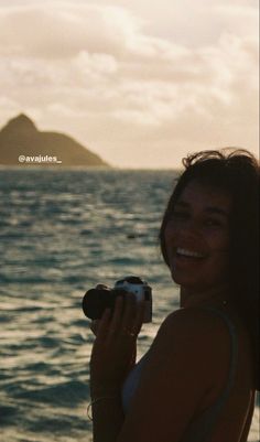 a woman holding a camera in front of the ocean with an island in the background