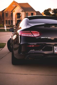 the back end of a black sports car parked in front of a house on a residential street