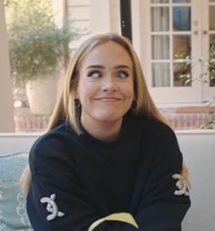 a woman sitting on a couch with her arms crossed and smiling at the camera while wearing a black sweater