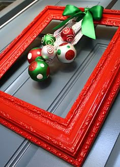 a red frame with christmas ornaments in it and a green bow on top is sitting on the floor