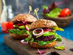 two burgers with lettuce, tomato and onion on a wooden cutting board