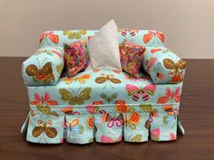 a blue couch with butterflies on it sitting on top of a wooden table next to a white pillow