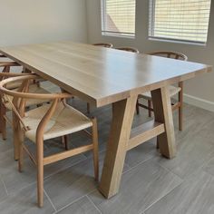 a wooden table with chairs around it in front of two windows and a tile floor