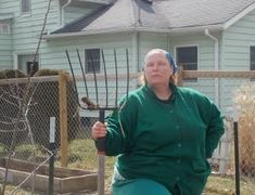 a woman in green jacket sitting on top of a wooden bench next to a fence