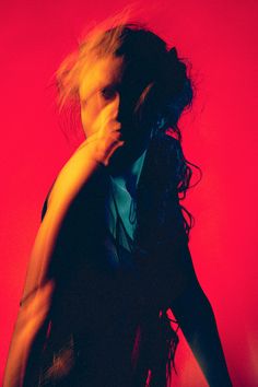 a woman with her hair blowing in the wind, wearing a black dress against a red background