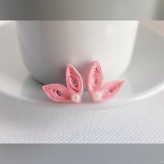 two pink butterfly shaped brooches sitting on top of a white plate next to a cup