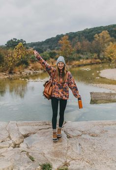 a woman standing on top of a rock next to a river with her arms in the air