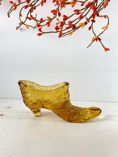 a yellow glass shoe sitting on top of a table next to a branch with red flowers