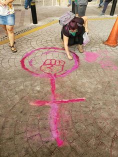 a woman kneeling down on the ground drawing with chalk